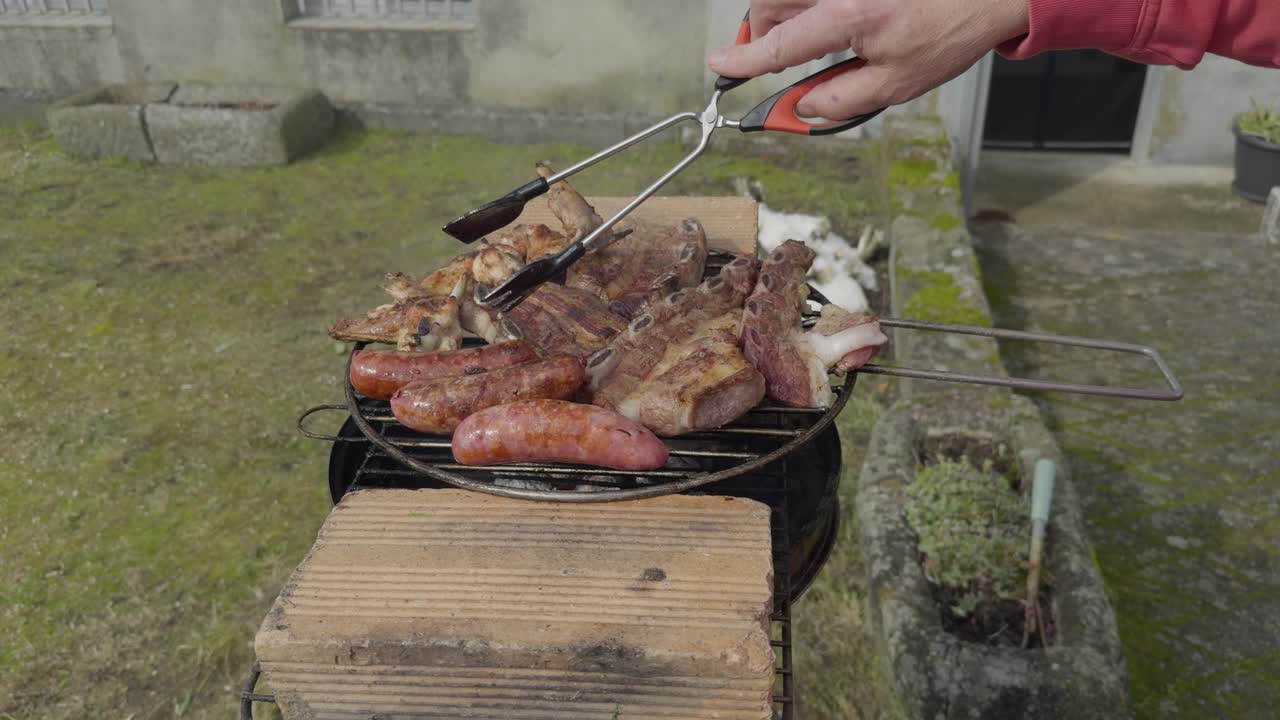 Kuřecí maso a klobásy, které se obrací při vaření kuchyňskými kleštěmi.