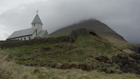 wide tilt down of a church and mountains in vidareidi, faroe islands