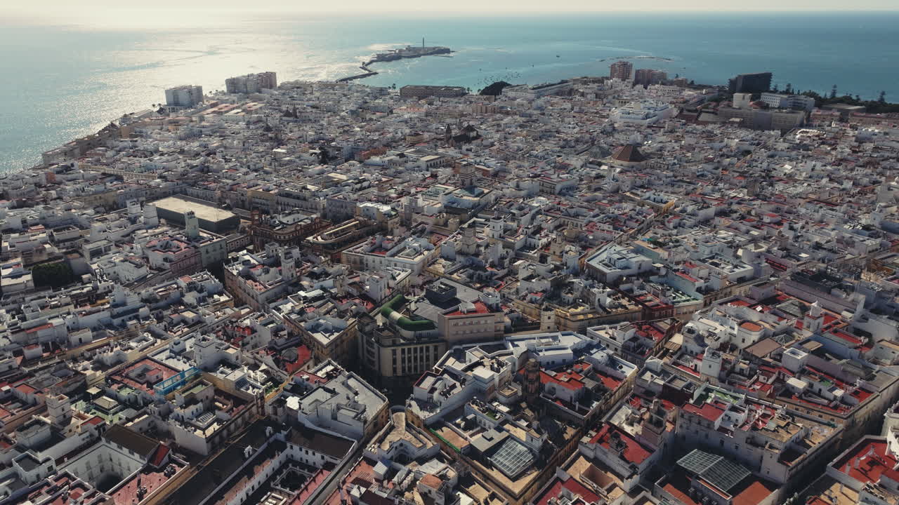 Plano aéreo cinematográfico ultra-amplo e estático da cidade de Cádis, cobrindo toda a península histórica e a paisagem urbana moderna de Cádis, cercada pelo Oceano Atlântico, na Espanha. Classificação de cinema
