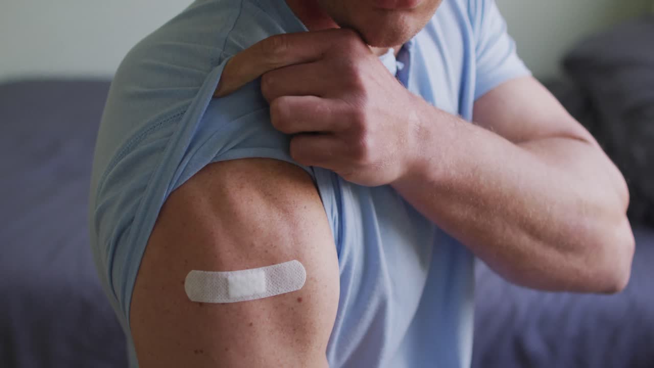 sección media de un hombre caucásico que muestra una venda en el brazo después de la vacunación contra la covid