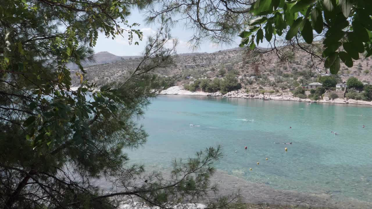 A nice view of the Aegean sea, shot through some trees. You can see people swimming in the water, and the nice colour that the sea has. Shot next to Alyki beach in Thasos, Greece.
