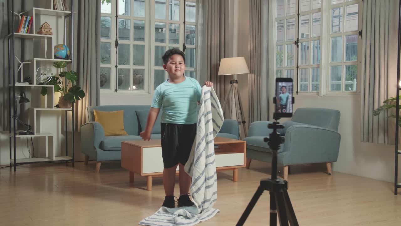 Asian Little Boy Shows Trick With Disappearing On Mobile Phone Camera While Recording On Smartphone Video Content For Social Networks In Cozy Room