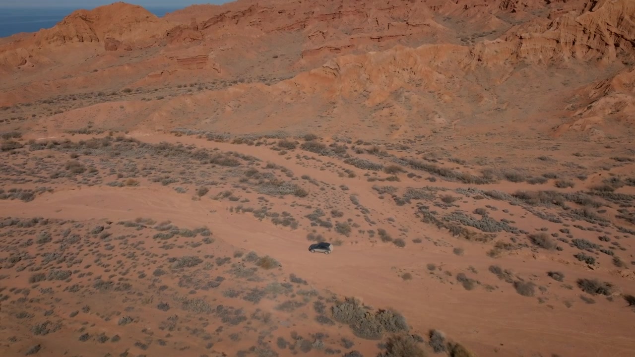 Riprese drone di scogliere di arenaria rossa e valle desertica arida con un'auto solitaria su una strada sterrata al Canyon di Marte, Regione di Issyk-Kul, Kirghizistan