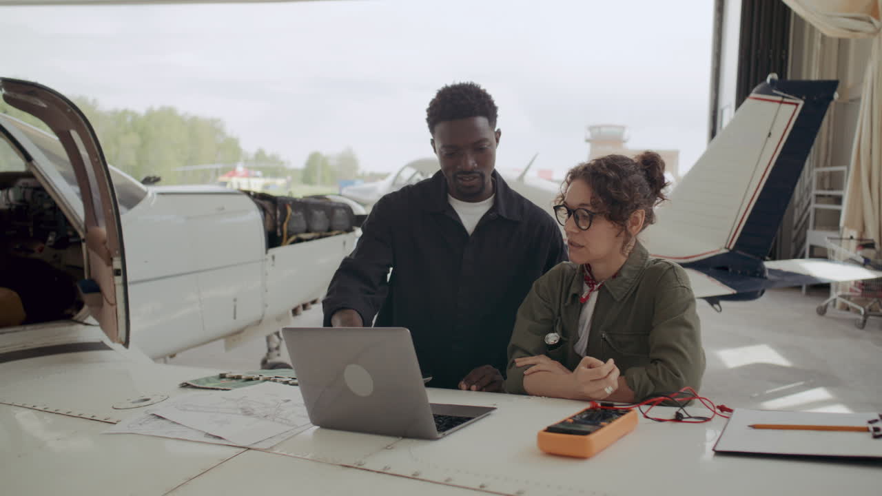 Colleagues Discussing Aircraft Repair Plan with Laptop and Papers in Hangar