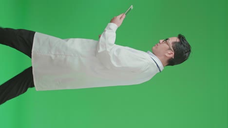 the side view of asian doctor with stethoscope wearing glasses and white coat using tablet while walking on green screen chroma key.