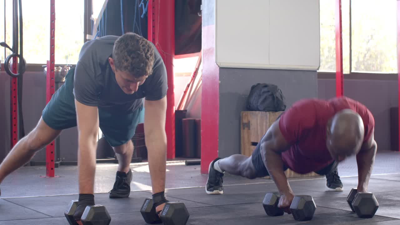 Diversos compañeros masculinos transicionando de flexiones a remos renegados, sosteniendo mancuernas hexagonales.