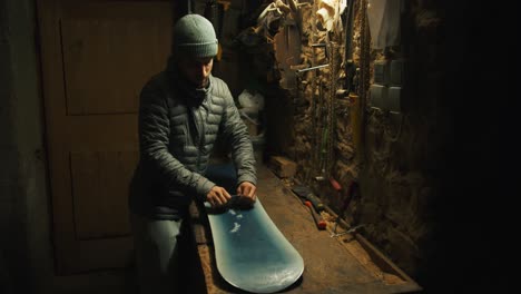 man starts scraping of wax of a snowboard