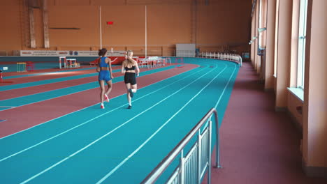 back view of two multiethnic female athletes running together on an indoor track