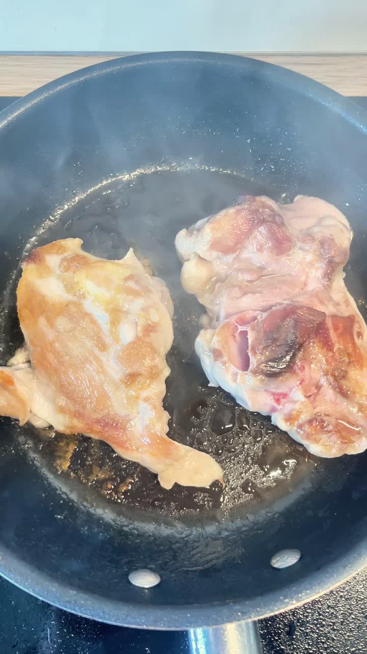 Due pezzi di carne cuociono in una padella. La padella è nera e la carne è marrone
