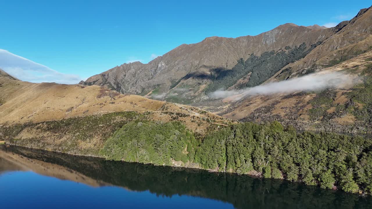 Aerial footage of Lake Moke with surrounding mountains under clear blue skies, showcasing tranquil natural beauty and reflection