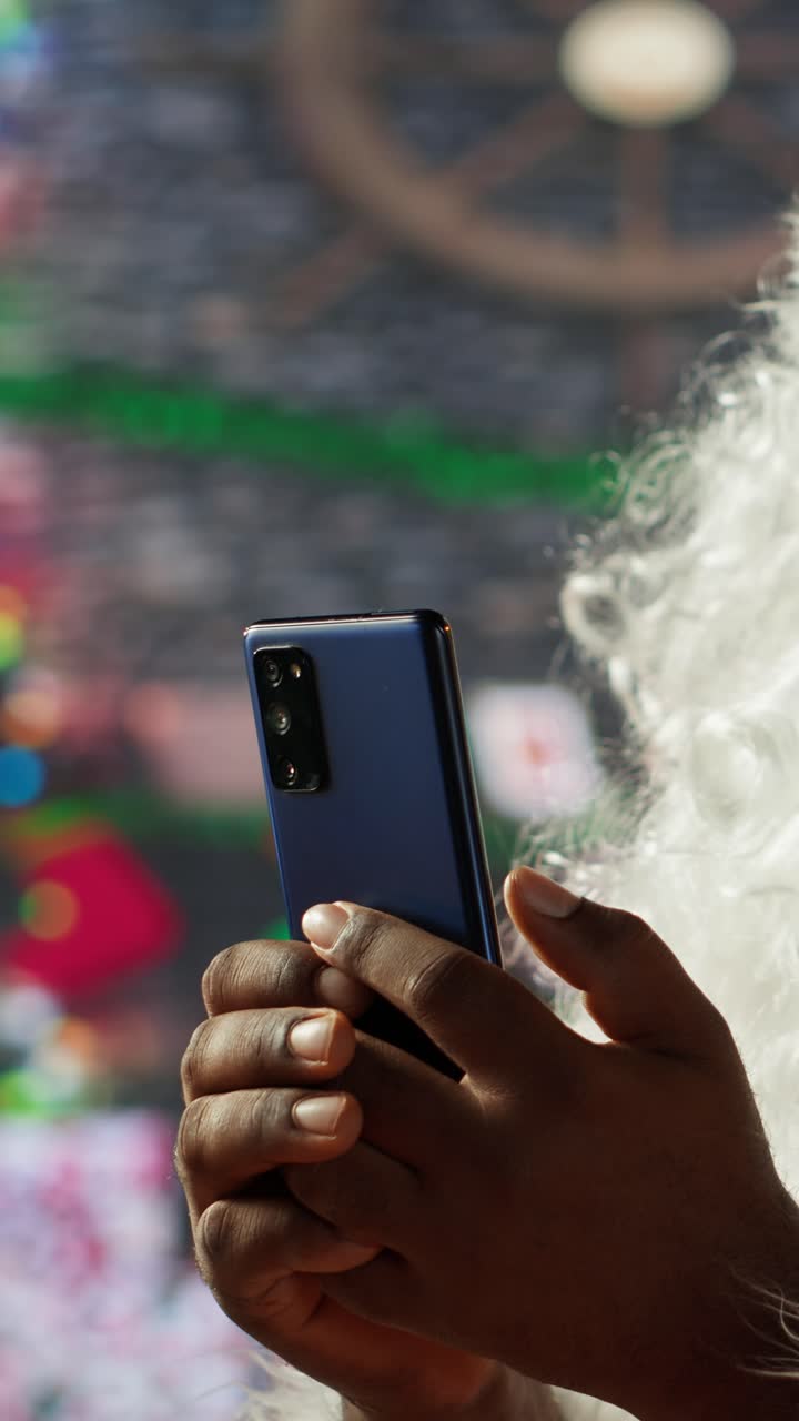 Osoba oblečená jako Santa Claus drží a používá chytrý telefon