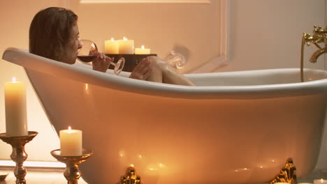 woman bathing with pleasure lying down in the tub with foam and drinking red wine spending time in luxury spa resort