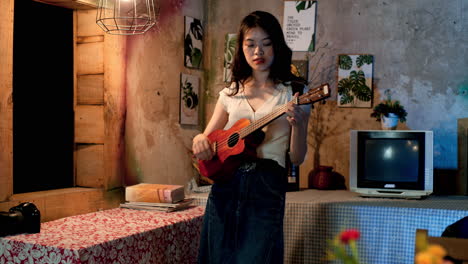 chica asiática tocando el ukulele en casa, estática