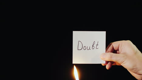 hand holds burning paper with inscription doubt