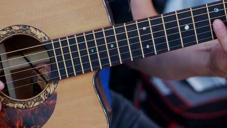 los dedos de un hombre blanco caucásico tocando una guitarra acústica y clavando un solo perverso, mientras la cámara se mueve de cerca en el tablero del traste