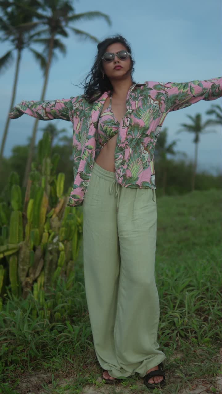 Woman in tropical print bikini and loose shirt outdoors in lush setting, vertical shot