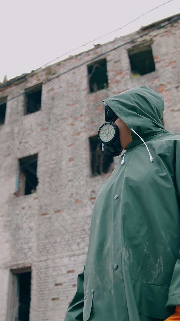 Consequences of chemical attack in the city. Human in safety suit and mask to breathe standing alone on the background of ruined building without windows. Vertical video