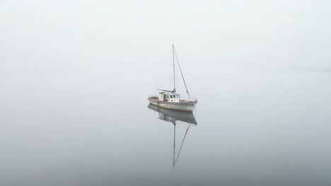 A solitary boat navigates through the misty waters, perfectly mirrored in the reflective surface, creating a serene atmosphere of tranquility and isolation