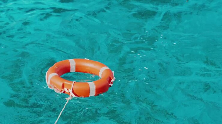 Orange and white lifebuoy life ring floating on rippling turquoise water with attached rescue rope