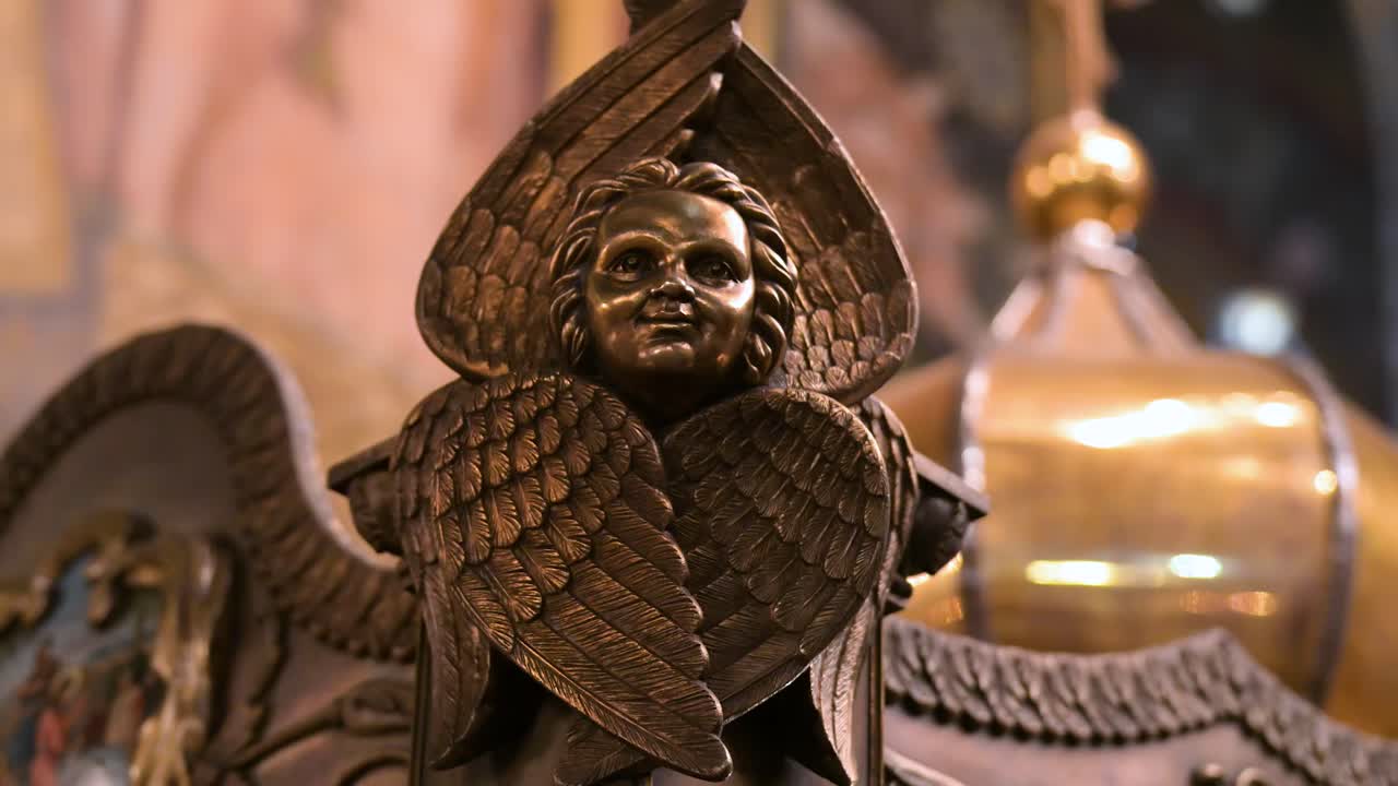 The detailed face and feathered wings of a cherub sculpture, a piece of sacred art within St. Volodymyr's Cathedral in Kyiv, Ukraine. This macro shot highlights the masterful carving of the ornament.