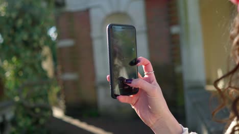 bella mujer con el pelo rizado tomando una foto con su teléfono móvil en una pérgola, a cámara lenta, en un día soleado