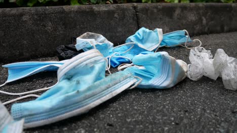 dirty discarded used corona virus masks blowing trash in wind on street sidewalk closeup slow dolly right