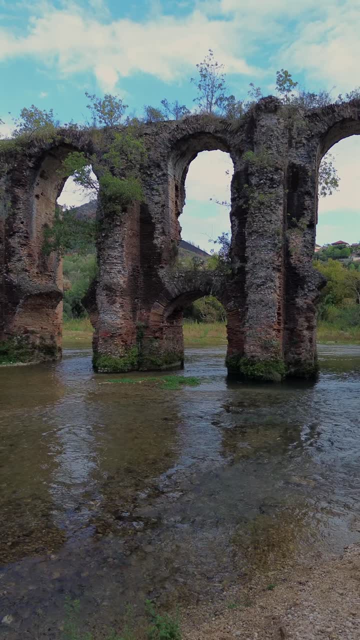Ripresa aerea verticale (pullback) con drone che rivela gli antichi archi dell'Acquedotto Romano di Nicopoli in Epiro, Grecia, con il panoramico fiume Louros e muratura storica, per contenuti di viaggio sui social media