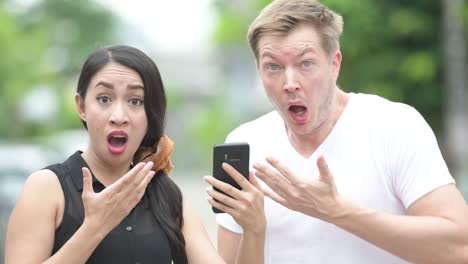 young multi-ethnic couple using phone together in the streets outdoors