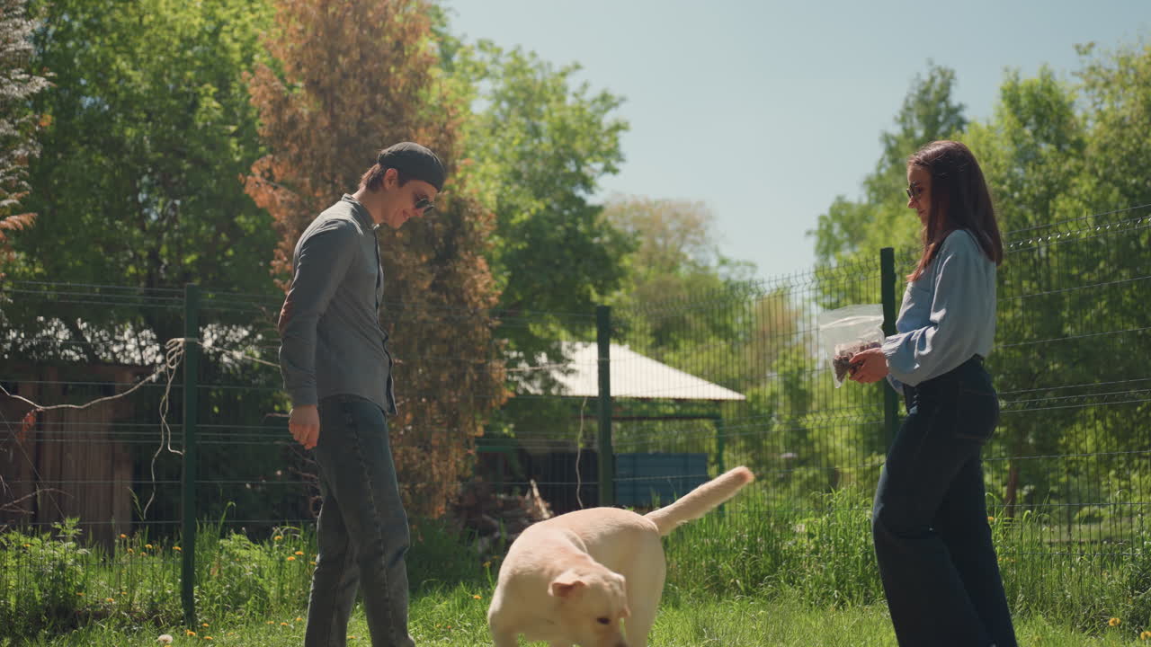 neighbors chatting outdoors, people interacting with their pet, couple and their dog in sunny yard, friendly neighbors converse casually next to their dog in cheerful garden setting