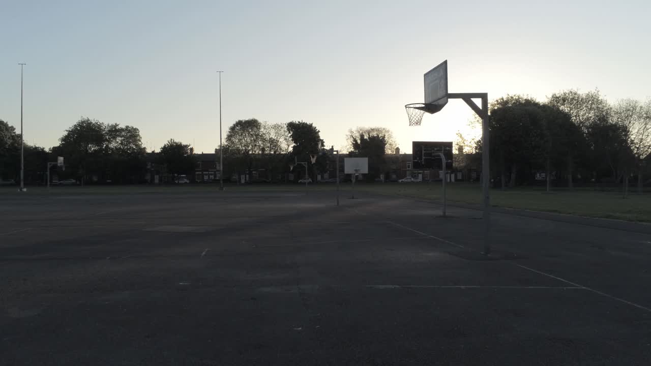 Sunrise shadow silhouette empty basketball court dolly low right passing net