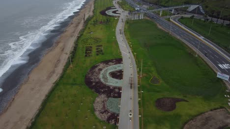 green grassy park with a long walkway by the ocean shore to the left and a freeway to its right