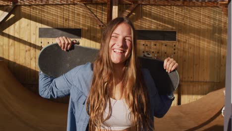 video de una feliz patinadora caucásica sosteniendo una patineta en un parque de patinaje