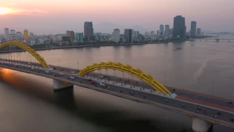 Amazing-colorful-wide-aerial-shot-of-iconic-Dragon-Bridge-Cau-Rong,-traffic-and-city-skyline-during-sunset-in-Danang,-Vietnam