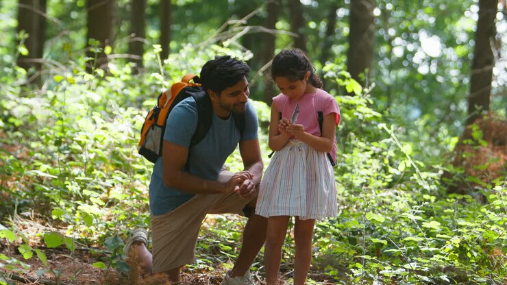 Father With Daughter Looking At Feather On Walk Through Summer Woodland Countryside