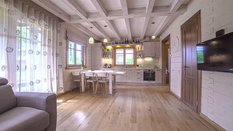 Pan-right-to-left-shot-of-white-trendy-moden-kitchen-along-with-dining-table-in-a-wooden-house-at-daytime