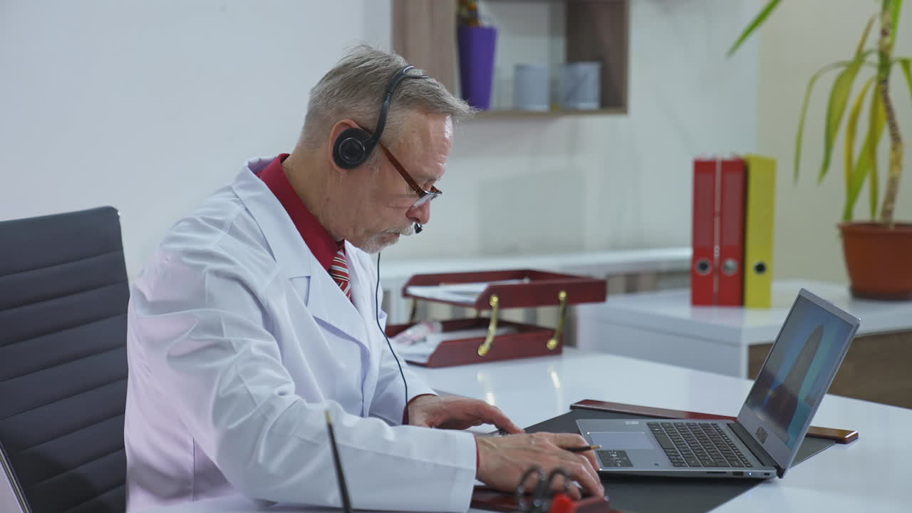Doctor writing an appointment for a client during video call. Professional doctor with headphones making online consultation through the laptop in medical center.