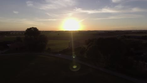 A-drone-shot-flying-upwards-and-panning-down,-with-the-sun-going-down-behind-a-church