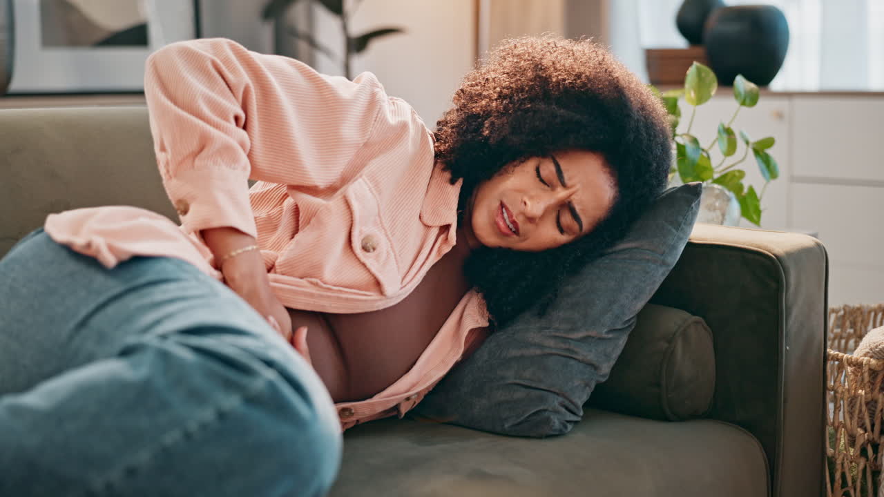 Woman experiencing abdominal pain lying on sofa