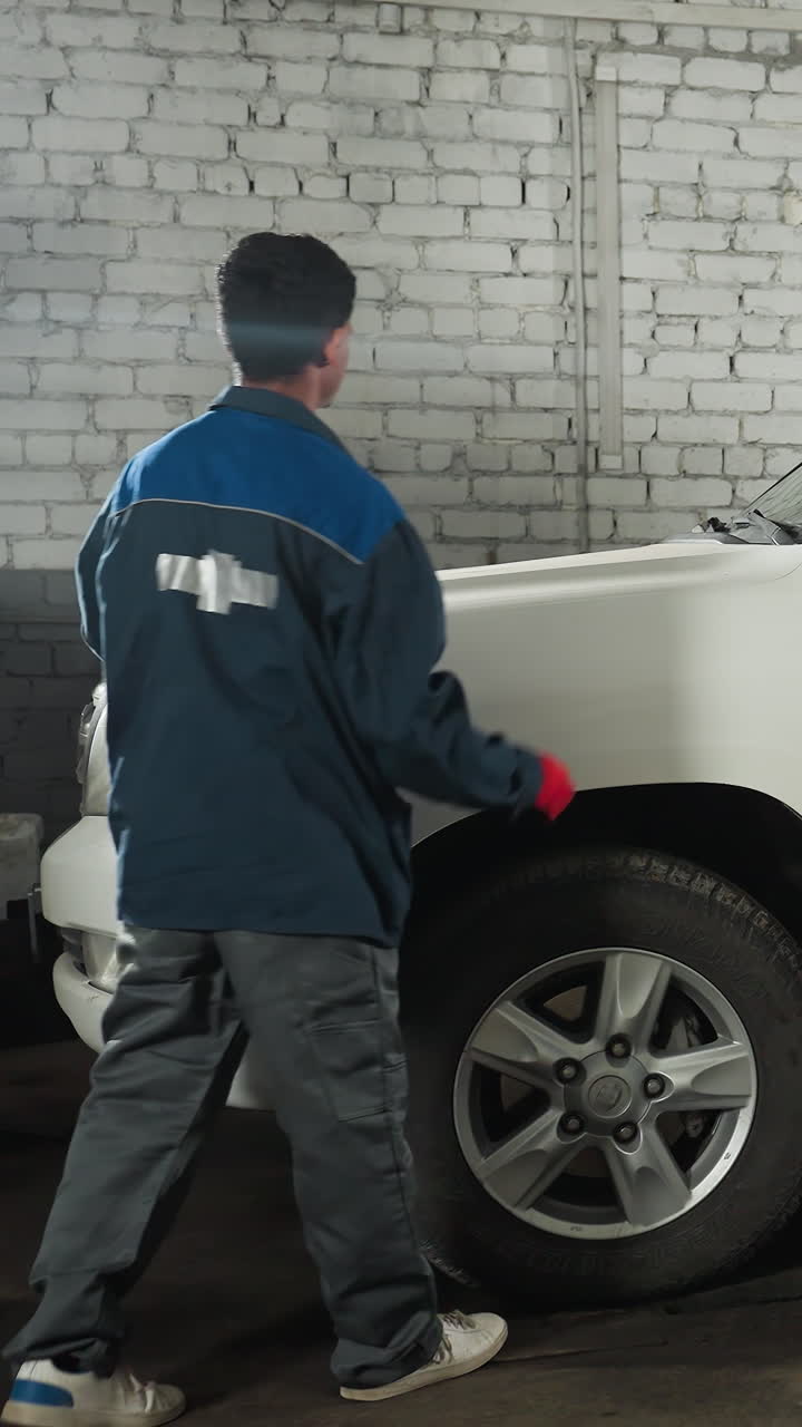mecánicos en uniformes azules inspeccionando los neumáticos de los automóviles en su taller usando una linterna para comprobar los daños, con el vehículo levantado en un ascensor en el fondo, reparación de automóviles en progreso
