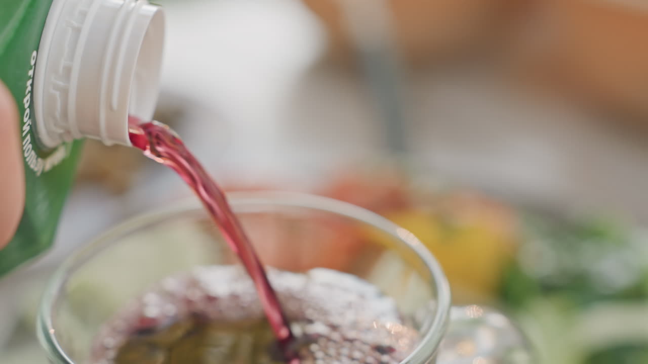 Una tazza da campeggio che si riempie di succo frizzante, un campeggiatore versa una bevanda rossa frizzante da una bottiglia in una tazza trasparente, bollicine che salgono e schiuma che si forma, insalata fresca e luce solare sullo sfondo, un vivace rinfresco all'aperto.