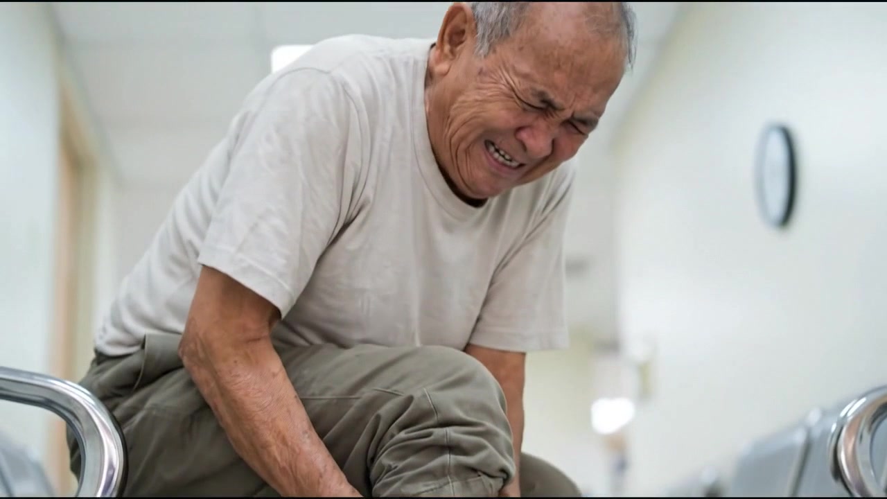 Seated adult rubbing sore wrist and hand inside bright home in everyday health concept