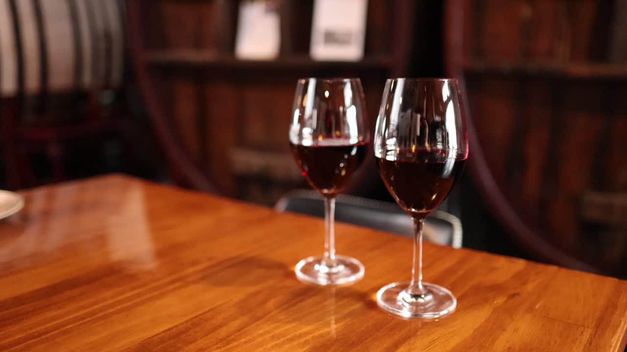 Vino rosso versato in due bicchieri su un tavolo di legno, illuminazione calda, sfondo rustico di una cantina vinicola