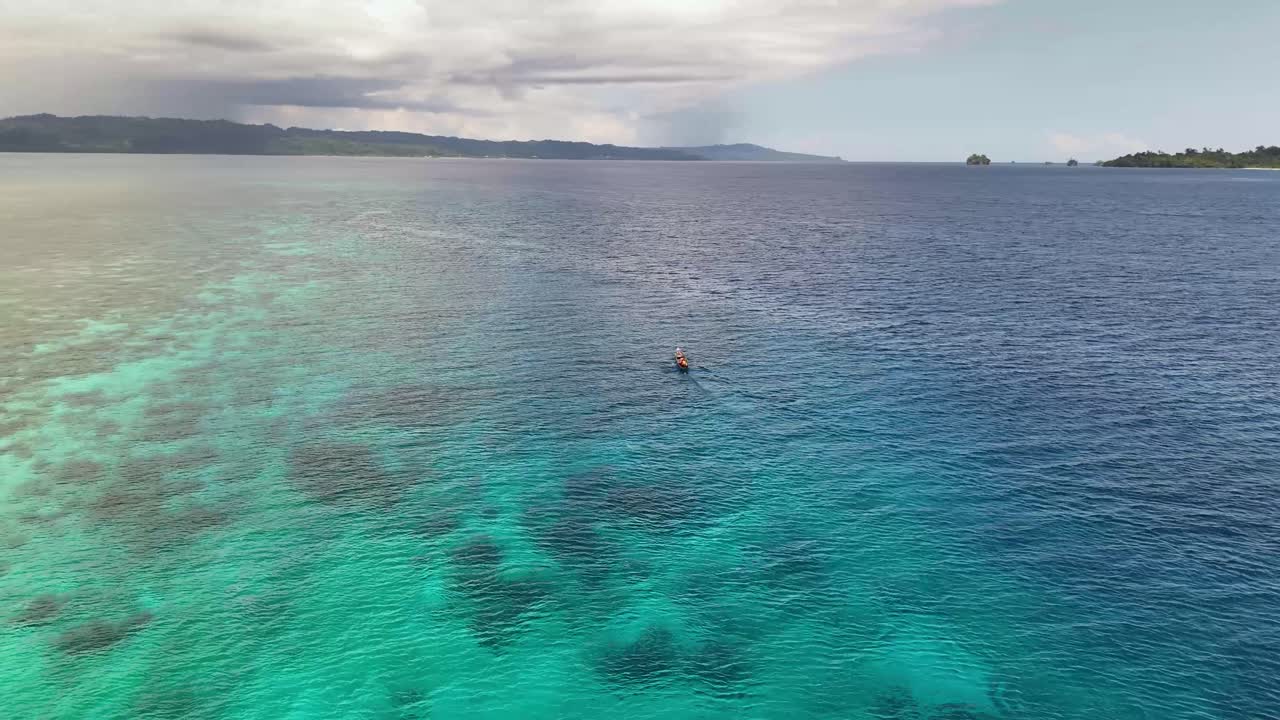 Video drone 4K che riprende una piccola barca da pesca che naviga attraverso le splendide acque blu dell'oceano. Si possono vedere isole tropicali sullo sfondo. Questo si trova nelle Isole Banggai a Sulawesi, Indonesia.