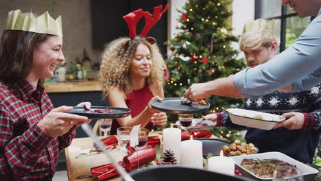 group of friends sitting around dining table at home as vegetarian christmas dinner is served