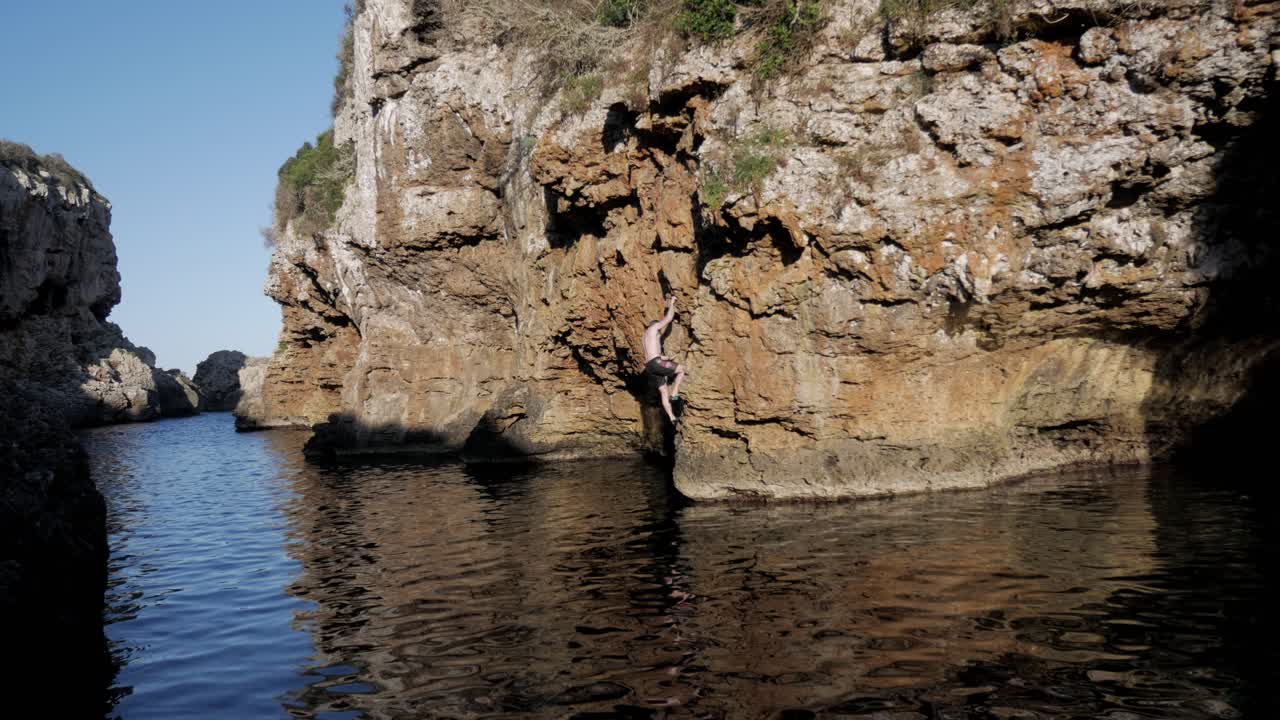 Climber on sea cliff, practicing deep water soloing at Cala Rafaelet, no rope
