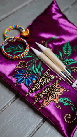 woman's hand decorating a traditional purple pillow with henna art and bracelets