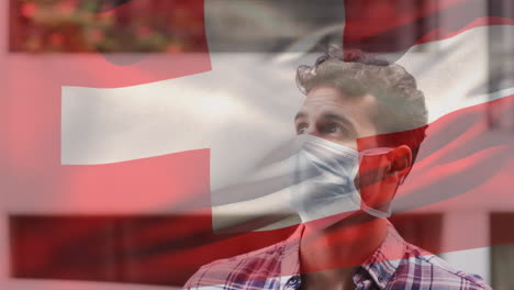 animation of flag of switzerland waving over man wearing face mask during covid 19 pandemic