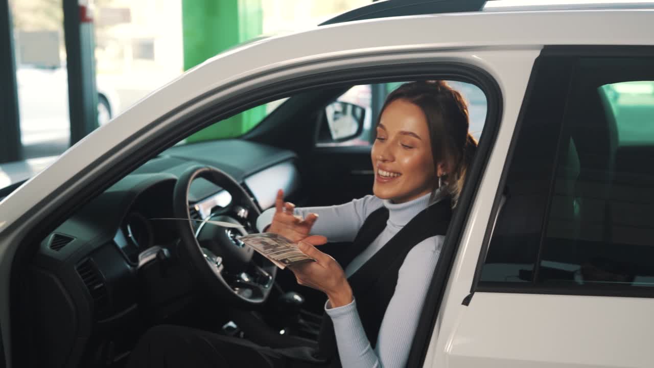 una mujer joven esparce billetes mientras está sentada en un auto