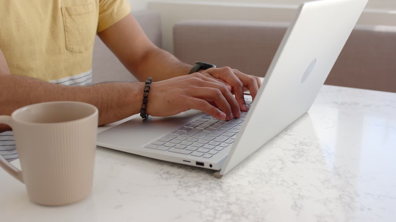 Man typing on silver laptop for work with soft light starting brightening scene, adjusting bracelet