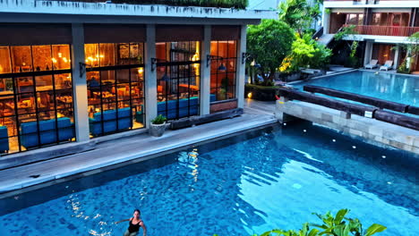 revealing shot of hotel with a woman relaxing in pool at pantai berawa, indonesia